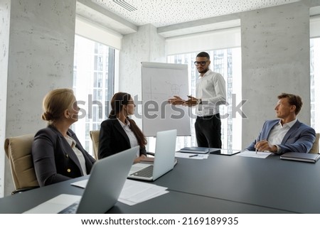 Diverse businesspeople gather in board room take part in group meeting, African boss holds briefing with employees, make presentation for clients on flip chart, partners negotiating in office concept 商業照片 © 