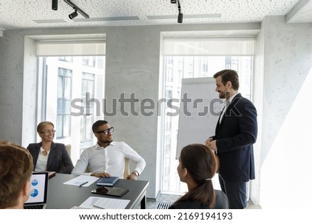 Group of multi ethnic people take part in meeting or negotiations led by businessman in suit standing in front of businesspeople make speech, gives presentation on flip chart. Training event concept 商業照片 © 