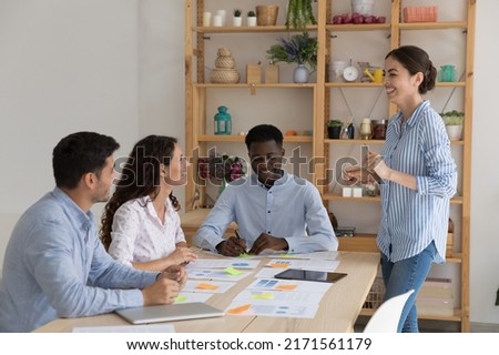 Cheerful female boss and diverse subordinates take part in morning briefing gathered in cozy board room. Teamwork, coaching, professional staff, employees workflow, sales statistics analysis concept 商業照片 © 
