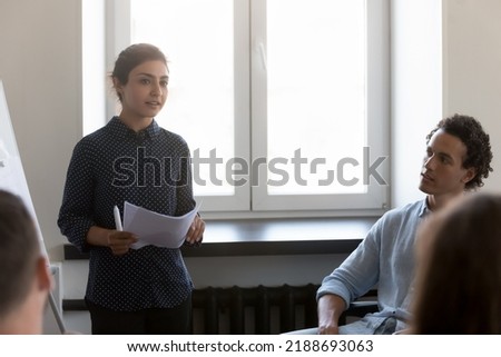 Indian project leader makes flip chart presentation for diverse businesspeople or company clients at formal meeting or negotiations in office. Employees listen to business coach take part in seminar 商業照片 © 