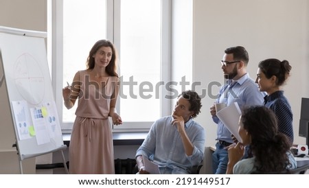 Business training event for corporate staff members concept. Multi ethnic businesspeople gathered in modern office take part in seminar lead by confident young coach makes presentation on flip chart 商業照片 © 