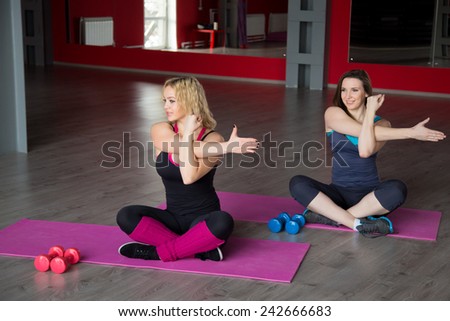 Two pretty female friends sit cross-legged doing aerobics exercises on mats in class in sports club