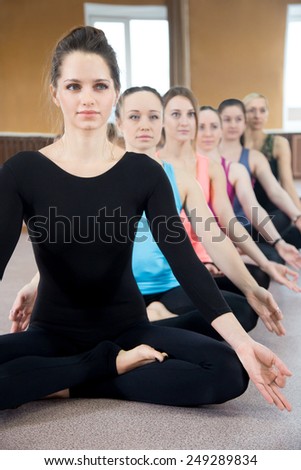 Sporty yogi girls doing fitness exercises in class, sitting in lotus position, Yoga pose sukhasana (Easy Pose, Decent Pose, Pleasant Pose)