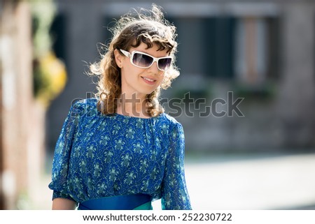 Happy smiling girl out on the walk on street, portrait of young female in sunlight with golden curly hair