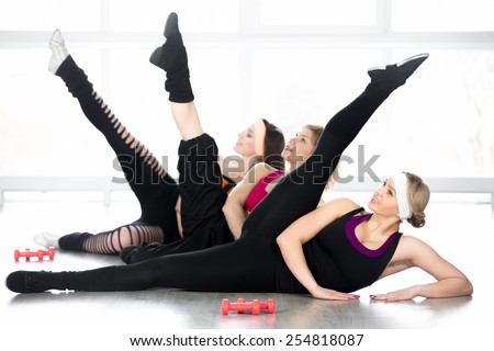 Fitness practice, group of three sporty females stretching, doing leg swings, exercises for flexibility, problem zones, hips, waistline, warming up during sport lesson in class