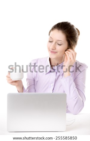 Young woman resting in front of computer enjoying music in earphones with closed eyes, relaxing with cup of coffee