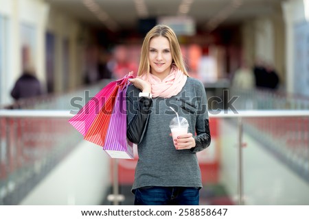 Smiling attractive teenage girl shopping in big store, carrying paper bags with purchases and milkshake