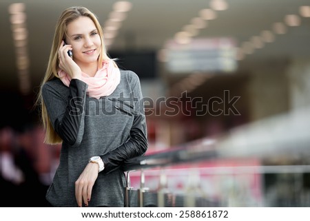 Smiling young woman in casual style clothes talking on mobile phone, making call, waiting for someone in contemporary large building, shopping center, station, copyspace