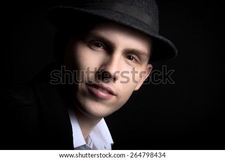 Portrait of smiling attractive young male model in hat with confident look, studio shot against black background