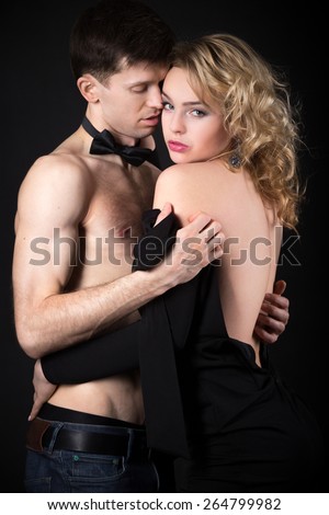 Steamy scene after party, beautiful young couple caught up in the middle of undressing before sex, woman in evening dress looking at camera, studio, black background