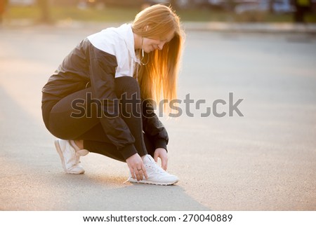 Young female tying laces on white sneakers on the street, jogger preparing for running workout. Healthy, active lifestyle concepts, copy space