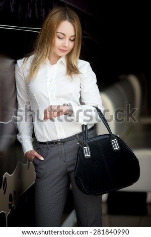 Cool attractive girl wearing modern office style outfit looking at watch, checking time, holding one hand in her pocket, waiting
