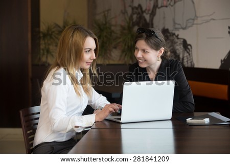 Two young caucasian women friends meeting, talking, sitting at the table beside laptop