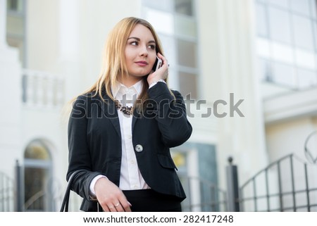 Beautiful young elegant office woman wearing formal outfit, walking on city street, using smartphone, making a call, not looking in camera, copy space