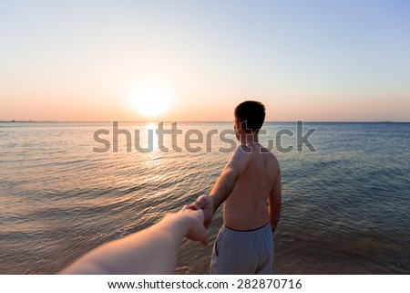 Young man leading by hand his lover, at the sea coast in sunlight, follow me concept
