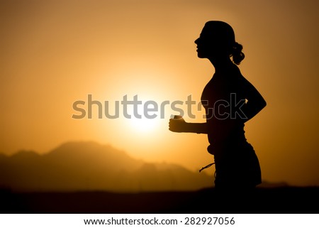 Profile silhouette of young sporty woman jogging against colorful picturesque mountainous landscape with rising or setting sun, copy space