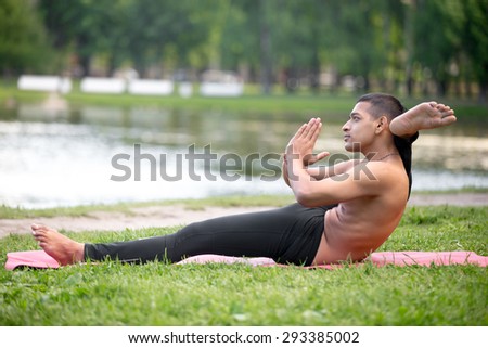 Profile of sporty handsome Indian young man working out on river bank in park, doing stretching exercises, Eka Pada Sirshasana, Foot behind the Head Pose, full length, hands in Namaste