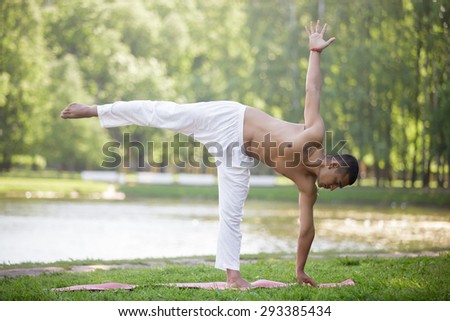 Serene attractive Indian young man in white linen clothes working out on lake in park, standing in ardha chandrasana (Half Moon Pose), full length