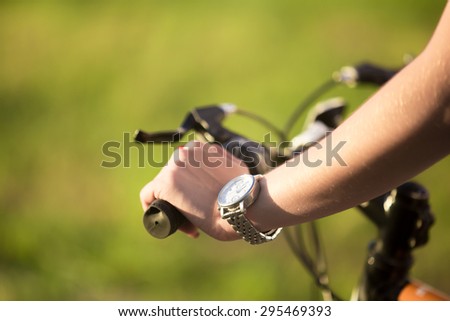 Beautiful sporty young woman hand griping bicycle handle in bright sunlight on summer day, close up
