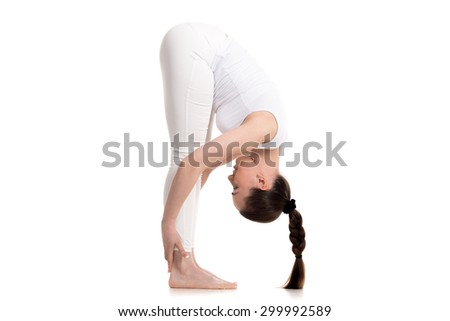 Sporty beautiful young woman in white sportswear with cute braid hairstyle doing Standing Forward Bend, Uttanasana pose, studio full length shot, isolated, part of Surya Namaskar series