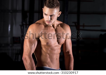 Portrait of young attractive caucasian athletic bodybuilder man working out in sports center, posing, showing abdominal and arm muscles, body sculpture concept