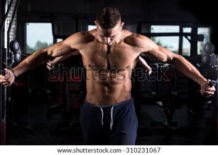 Portrait of young good looking caucasian muscular man working out in sports center, doing chest muscles training on crossover machine in gym, body sculpture concept