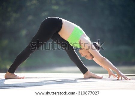 Beautiful sporty fit blond young woman in green sportswear working out outdoors, standing in Pyramid Pose, Intense Side Stretch Posture, Parsvottanasana, full length