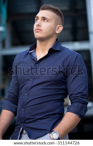 Portrait of young handsome stylish man wearing blue shirt standing on the street with hand in his pocket