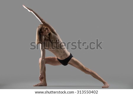 Sporty muscular young yogi man doing lunge exercise, standing in Extended Side Angle Posture, Utthita Parsvakonasana, studio shot on dark background, profile view, full length
