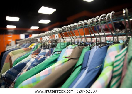 Hangers with colorful male shirts in fashion mall, close up