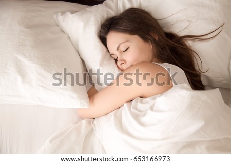 Top view of attractive young woman sleeping well in bed hugging soft white pillow. Teenage girl resting, good night sleep concept. Lady enjoys fresh soft bedding linen and mattress in bedroom  ストックフォト © 