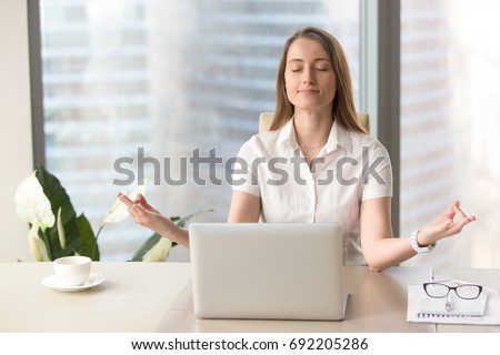 a female professional meditating in front of her laptop at work