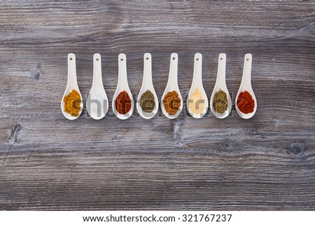 eight ceramic spoons lined up in a line filled with colorful spices on artificial wooden table