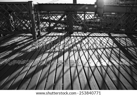 A black and white photograph of shadows and lines crossing the wooden path of the Brooklyn Bridge in New York City.