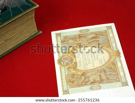 Historical, old Polish notes, bills (1919 - 1940) on the red carpet background next to the old book. Focus on some part of the image only, rest is blur by intention.