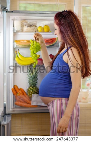 Pregnant woman standing in front of an open fridge