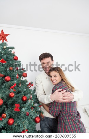 Happy couple hugging himself beside the christmas tree