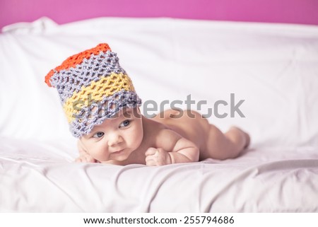 nice little girl lying on her stomach on the bed, blue eyes, and fun to knit cap on his head.
