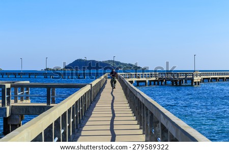 running man with nice view of long cement bridge walk way run on the blue sea with black shadow in blue sky sunshine day