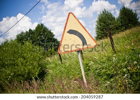 Left turn sign with rural scenic background.