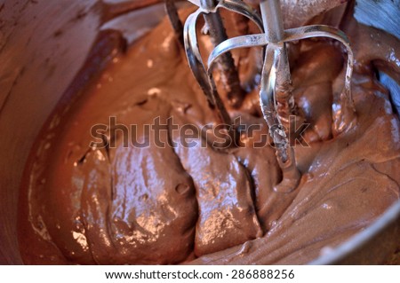 Closeup of chocolate cake mix in stainless still bowl with stainless steel beaters in mix. Cake is mixed and ready to be poured into baking pans.