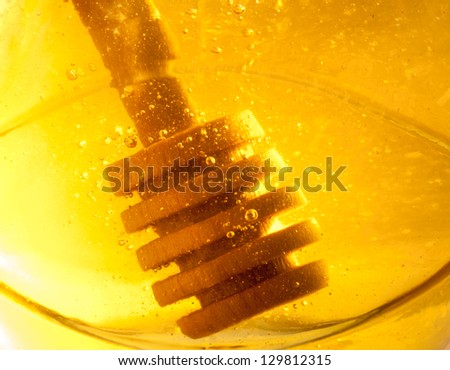 Bee honey with wooden dipper - healthy nutrition. Honey\'s dessert in a glass jar. Honey stick at golden honey background.