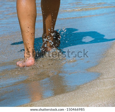 Guy is walking on the beach - bare feet with sea water spray. Healthy lifestyle - barefoot walk on the sand in summer day.
