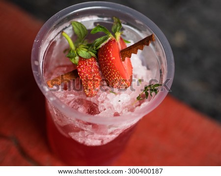 Strawberry frozen cocktail in a plastic glass with ice and a cocktail straws on blured background. Summertime bar menu with a cold drinks and fresh berry.