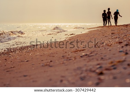 Silhouettes of group students walking on a sand beach in summer evening - romantic seascape at sunset with soft focus.