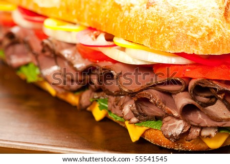 Large roast beef sandwich with cheese, lettuce, tomatoes, onion, red and yellow peppers.