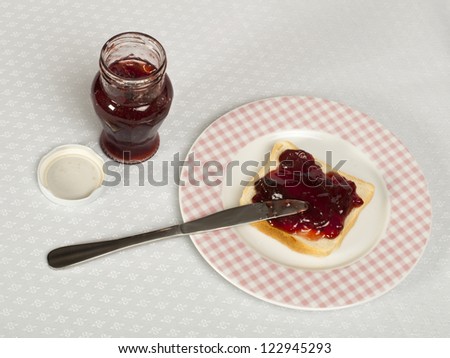 Spread jam on bread with knife and jar of jam. Pink checkered plate