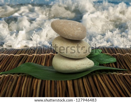Stacked stones on wooden base for spa and green leafs. Waves on the background.