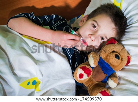 Sick child in bed with teddy bear. Measuring the temperature with a thermometer.