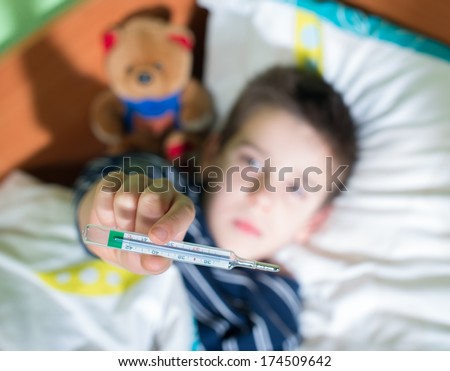 Sick child in bed with teddy bear. Measuring the temperature with a thermometer.